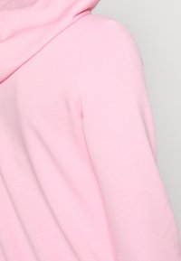 Jasnoróżowy sweatshirt z kapturem. Miękka, gładka tekstura i dopasowany krój. Wyposażony w kieszeń typu kangur i prążkowane mankiety.