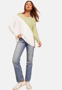 Zeleni in beli barvni razdeljen dolg rokav s pazduho ter V-izrezom, v kombinaciji z modrimi naravnost krojenimi kavbojkami in belimi supergami. Sproščen dizajn, mehak material.