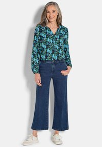 Langarmbluse mit einem blauen und schwarzen abstrakten Muster, kombiniert mit weiten, dunklen Jeans und weißen Sneakern.