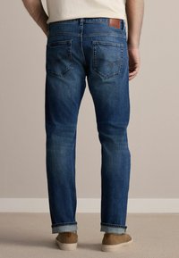 Vaqueros de mezclilla en un azul de lavado medio con corte recto, que cuentan con un diseño de cinco bolsillos, costuras visibles y dobladillos remangados. Parche de cuero en la cintura.