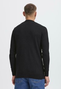 Schwarzer Pullover mit langen Ärmeln aus weichem Strickstoff. Verfügt über einen Rundhalsausschnitt und gerippte Bündchen sowie einen geraden Saum.