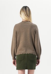 Brun strikkegenser med lange ermer, bølget halslinje og teksturert hem. Kombinert med et grønt kordfløyelskjørt som har to baklommer.
