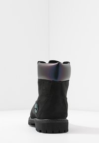 Schwarze Wildleder-Stiefelette mit glänzendem schwarzen Obermaterial, Gummisohle und farbigem Markenlogo. Verfügt über verstärkte Nähte und einen strukturierten Kragen.