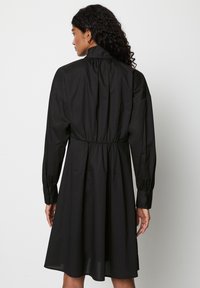 Schwarzes Baumwollkleid mit langen Ärmeln, gerafftem Ausschnitt und elastischem Bund. Verfügt über geknöpfte Manschetten und ein ausgestelltes Rockdesign.