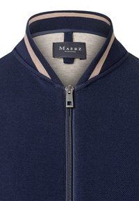 Giacca a zip navy con un design a maglia testurizzata, colletto a coste a righe beige in contrasto e una zip argentata. L'etichetta riporta "Maerz Muenchen."