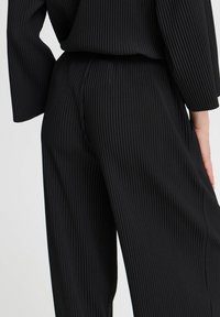 Pantaloni in tessuto a coste neri con gamba ampia e vita elasticizzata, che evidenziano la texture verticale su tutto il capo.
