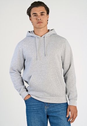 Grijze hoodie van zacht, textuurstof. Voorzien van een trekkoordkap, een buidelzak en geribde manchetten. Gecombineerd met blauwe denim jeans.