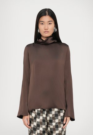 Bruine satijnen blouse met lange mouwen en een colhals. De stof heeft een gladde textuur en wordt gecombineerd met geblokte broeken.