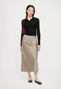 Svart langermet poloshirt, beige sateng midi skjørt, svarte ballettsko, og en liten rød crossover bag. Jevne teksturer, tett passform.