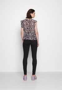 Blusa com estampado floral e mangas em babados, fundo preto e detalhes em roxo, combinada com jeans skinny pretos e sapatos de plataforma lavanda.