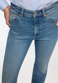 Jeansy z wysokim stanem w niebieskim denimie z lekkim rozszerzeniem, z pięcioma kieszeniami, pomarańczowymi szwami i srebrnym zapięciem na guzik w talii.