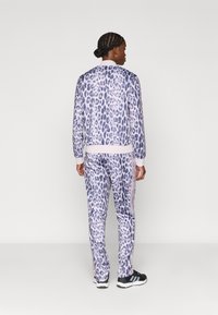 Ensemble de survêtement imprimé léopard en violet clair et blanc, avec une coupe décontractée, des poignets côtelés et un pantalon assorti avec des rayures latérales.