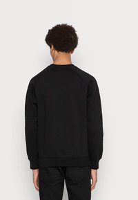 Felpa nera con collo a giro e maniche raglan. Realizzata in tessuto morbido, con polsini e vita a coste. Senza loghi visibili.