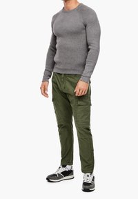 Pullover en tricot gris, pantalon cargo vert olive avec poches, et baskets noir et blanc avec des accents texturés. Coupe décontractée et design moderne.