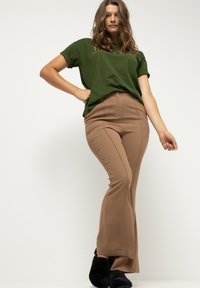 Camiseta verde de manga corta sobre pantalones marrones de campana, con una textura suave y costuras delanteras, combinados con calzado negro.