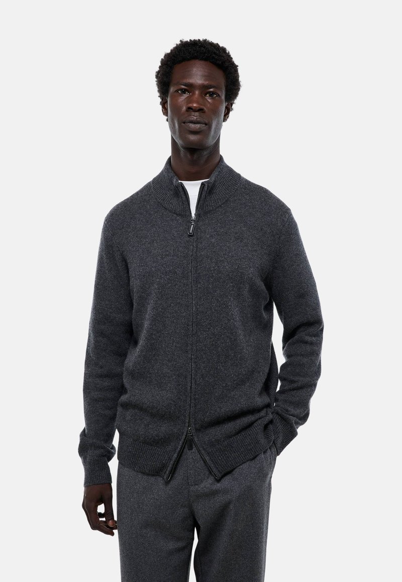 Sweatshirt zippé gris avec un col haut, fabriqué en tissu doux. Détails notables comprenant des poignets et un ourlet côtelés, ainsi qu'un design épuré et minimal.
