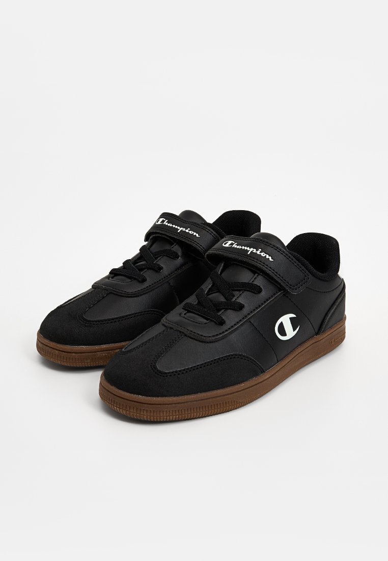 Baskets basses noires avec des semelles brunes, à lacets à l'avant et à bandes velcro, marquées "Champion" avec un logo "C" blanc sur le côté.