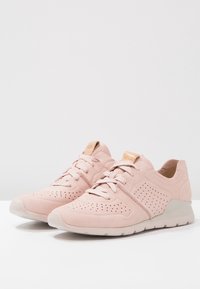 Světle růžové sportovní boty vyrobené z texturovaného materiálu, s perforacemi, nízkoprofilovým designem a bílou gumovou podrážkou.