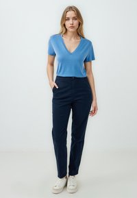 Niebieski T-shirt w kształcie V sparowany z granatowymi spodniami. T-shirt jest lekki, o gładkiej fakturze. Spodnie mają prosty krój z kieszeniami, noszone z białymi sneakersami.