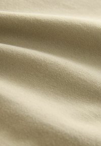 Beiger Baumwollstoff mit einer glatten, weichen Textur, die subtile diagonale Webmuster und sanfte Falten über die Oberfläche zeigt.