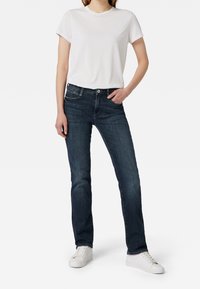 Camiseta blanca de manga corta combinada con jeans azul oscuro. Los jeans tienen un corte clásico, cinco bolsillos y detalles de costura sutiles. Zapatillas blancas completan el look.