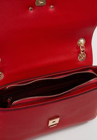 Borsa a mano rossa con superficie testurizzata, dettagli dorati e interno con zip. Presenta una chiusura rettangolare e dettagli in catena.