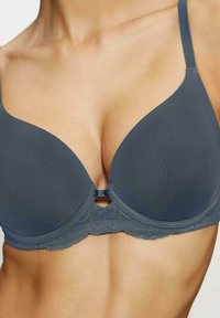 Szary stanik z drutem, wykonany z formowanej tkaniny, z koronkowym wykończeniem, regulowanymi ramiączkami i ozdobną kokardką na środku. Gładka tekstura tkaniny.