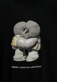 Camiseta negra con un gráfico bordado de dos personajes de dibujos animados abrazándose, en tonos gris claro y beige, y el texto "MWM x mod wave movement".