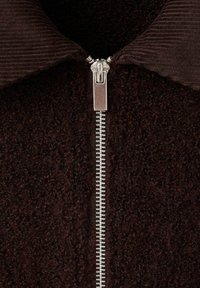 Bruine textuurjasje met een metalen rits die in het midden loopt, voorzien van een corduroy kraag en pluizige stof.