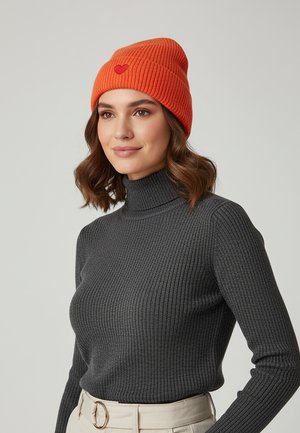 Bright orange ribbed beanie with a small red heart detail, worn with a dark gray ribbed turtleneck sweater. Neutral background.