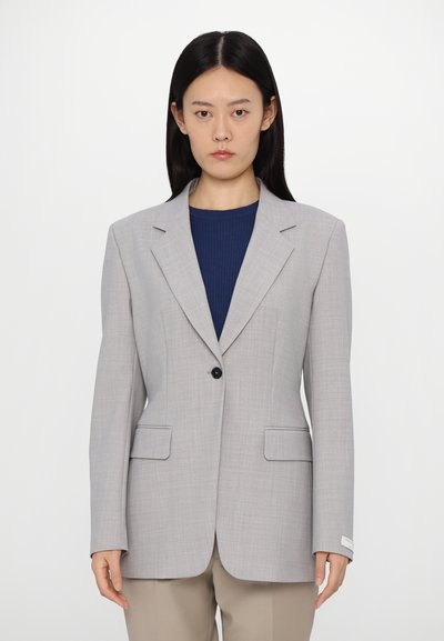 Hellgrauer Blazer mit maßgeschneidertem Design, Reverskragen, einem schwarzen Knopf und zwei Fronttaschen. Glatte Textur mit dezentem Muster.