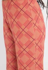 Nohavice v kockovanom vzore so červenou, oranžovou a krémovou farbou, s jemnými líniami a textúrovanou tkaninou. Slim fit silueta.
