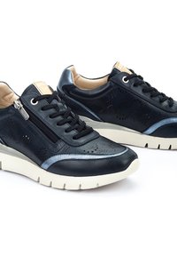 Černé kožené sneakers s perforovaným designem, šedými kovovými akcenty a bočním zipem. Silná bílá podešev zajišťuje stabilitu a pohodlí.
