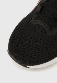 Svart treningssko med teksturert mesh-overdel, rundet tå og hvit såleliste. Snøring i mørk farge er festet til en støttende overlay.