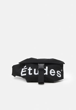 Marsupio in tessuto nero con chiusura frontale a fibbia e logo bianco "Études" sul davanti, su sfondo bianco uniforme.