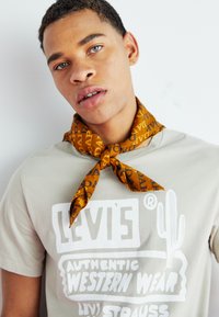 Beige t-shirt with white graphic text featuring "Levi's" and a cactus, paired with an orange patterned scarf tied around the neck.