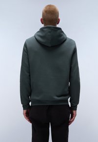 Sudadera verde oscura con una textura suave y capucha ajustable, presenta puños y cintura de canalé, mostrada desde la parte de atrás, combinada con pantalones negros.