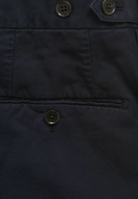 Marine stof met een gladde textuur, voorzien van twee donkere knopen en een klein pocketdetail, verticaal uitgelijnd aan de linkerkant.