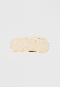 Pantofola beige con una parte superiore in morbida pelliccia e suola in gomma texturizzata. La suola presenta un design a motivi per una migliore aderenza.