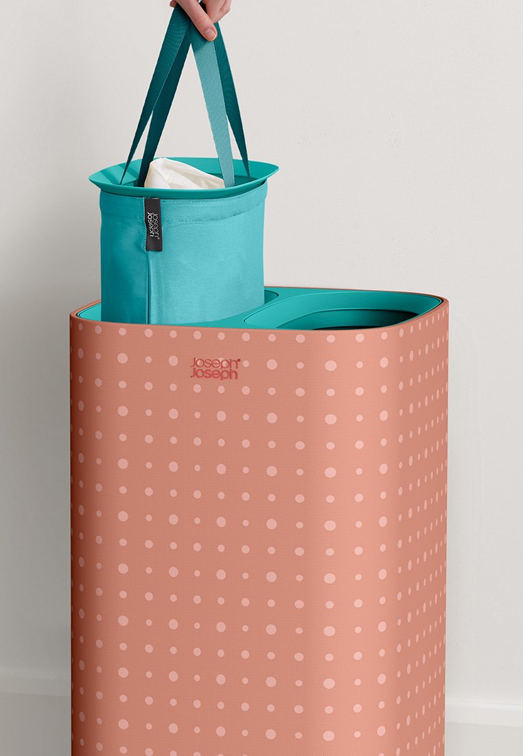 Müllbehälter mit zwei Fächern, außen in korallenrosa mit Punkten und einem inneren Teilt in Teal. Verfügt über stabile Griffe und ein schlankes, modernes Design.