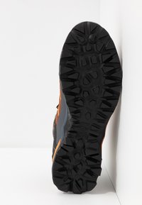 Semelle noire texturée avec des motifs profonds, arborant des accents orange et gris. Le design met l'accent sur l'adhérence et la stabilité pour les activités de plein air.