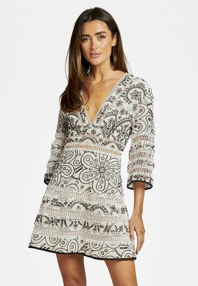 Vestido blanco con intrincados bordados florales negros, mangas tres cuartos, escote en V profundo y detalles de encaje texturizado a lo largo del dobladillo.