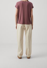 Bordeaux kortärmad topp med vågformad halsringning, ihopparad med krämfärgade vida byxor och bruna skor som har vita och blå ränder.