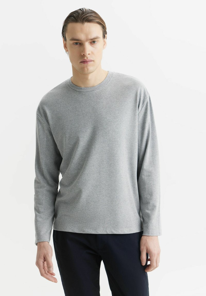 Szara koszulka z długim rękawem, uszyta z miękkiego i lekkiego materiału, wzorowana na klasycznym dekolcie. Gładka tekstura z minimalnymi detalami szwów.