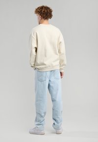 Sudadera de cuello redondo beige claro combinada con jeans holgados de color azul claro. El conjunto tiene un ajuste relajado y se complementa con zapatillas blancas.