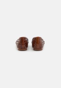 Chaussures en cuir tressé marron à enfiler avec une semelle plate, présentant une finition texturée et un dos arrondi. Design simple avec des accents minimaux.
