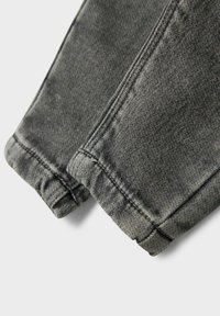 Sivi denimski materijal s lagano istrošenom teksturom, koji prikazuje uredno presavijen rub i kontrastne šavove.
