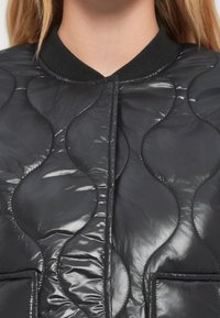 Κοντινό πλάνο μαύρου γυαλιστερού καπιτονέ μπουφάν με ραφές σε κυματιστό μοτίβο και ριμπ κολάρο σε άτομο.