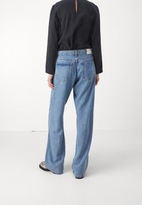 Světle modré, vysoce pasové džíny s uvolněným střihem, s dvěma zadními kapsami a viditelným švem. Kombinované s černým topem.