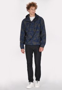Hanorac cu glugă de culoare albastru închis, cu un model de camuflaj texturat, asortat cu blugi negri și adidași albi.